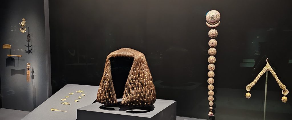 (Middle) Large and small wig rings of Sithathoryunet, on a modern wig 
Egypt, Middle Kingdom period, 12th Dynasty, 
reign of Senwosret II–Amenemhat III, about 
1887–1813 BCE Gold 
From Egypt, Lahun, (Right) Plait ornament (Jadanagam), Attributed to India, probably Madras, 18th to 19th century, Gold with rock crystal, rubies, emeralds and amethyst inlays, (Far Right) Head ornament, Attributed to India, Kashmir, Punjab or Rajasthan, 19th century, Gold, glass, turquoises, Global Jewellery