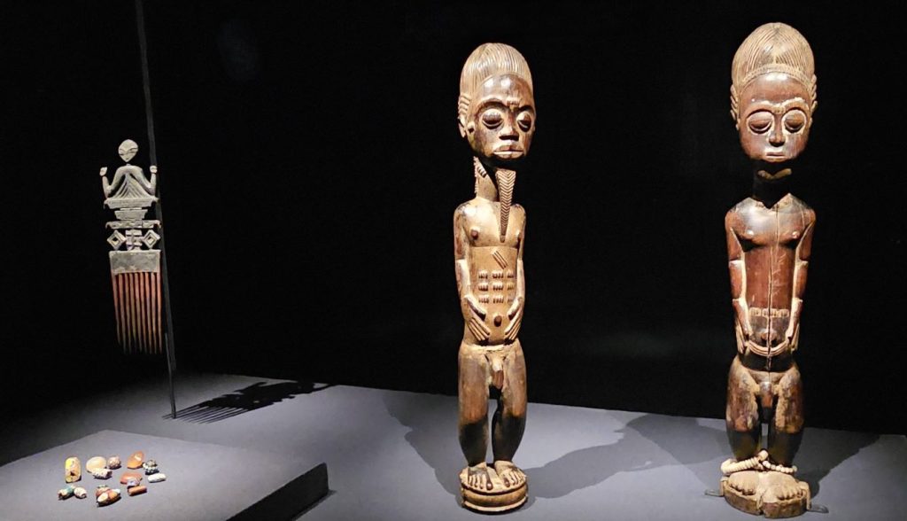(Top Left) Duafe (comb), Ghana, Akan peoples, 19th to mid-20th century, Wood, The Michael C. Rockefeller Memorial Collection, gift of William W. Brill, 1963, The Metropolitan Museum of Art, New York
(Bottom Left) Beads, For the Afro-Eurasian trade,16th to 19th century, Glass, stone, The Metropolitan Museum of Art, New York
(Right) Male figure, Central Cote d’Ivoire, Baule peoples, 19th to mid-20th century, Wood, Gift of Mr and Mrs Brian S Leyden, 1983, The Metropolitan Museum of Art, New York
(Far Right) Male figure, Central Cote d’Ivoire, Baule Peoples, 19th to mid-20th century, Wood, glass beads, plant fibre, The Michael C. Rockefeller Memorial Collection, bequest of Nelson A. Rockefeller, 1979, The Metropolitan Museum of Art, New York, Global Jewellery
