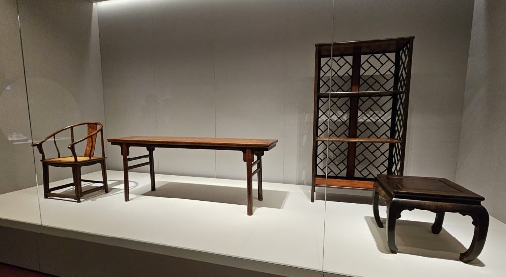 From Left: Horseshoe armchair and Pingtouan table, Late Ming dynasty, late 16th century to mid-17th century, Huanghuali wood, Gift of Grace Wu Bruce, Hong Kong Palace Museum
Right: Lattice-backed shelf, Ming dynasty (1368-1644), Zitan wood, The Palace Museum
Far Right: Stool, Late Ming to early Qing dynasty, 17th century, Zitan wood, The Palace Museum, Forbidden City and the World